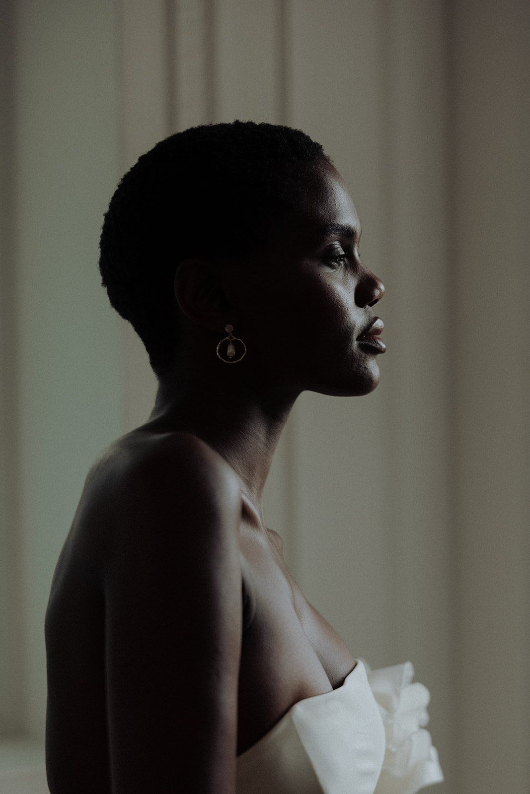 Bride in couture gown wearing luminous earrings, soft profile editorial bridal portrait.