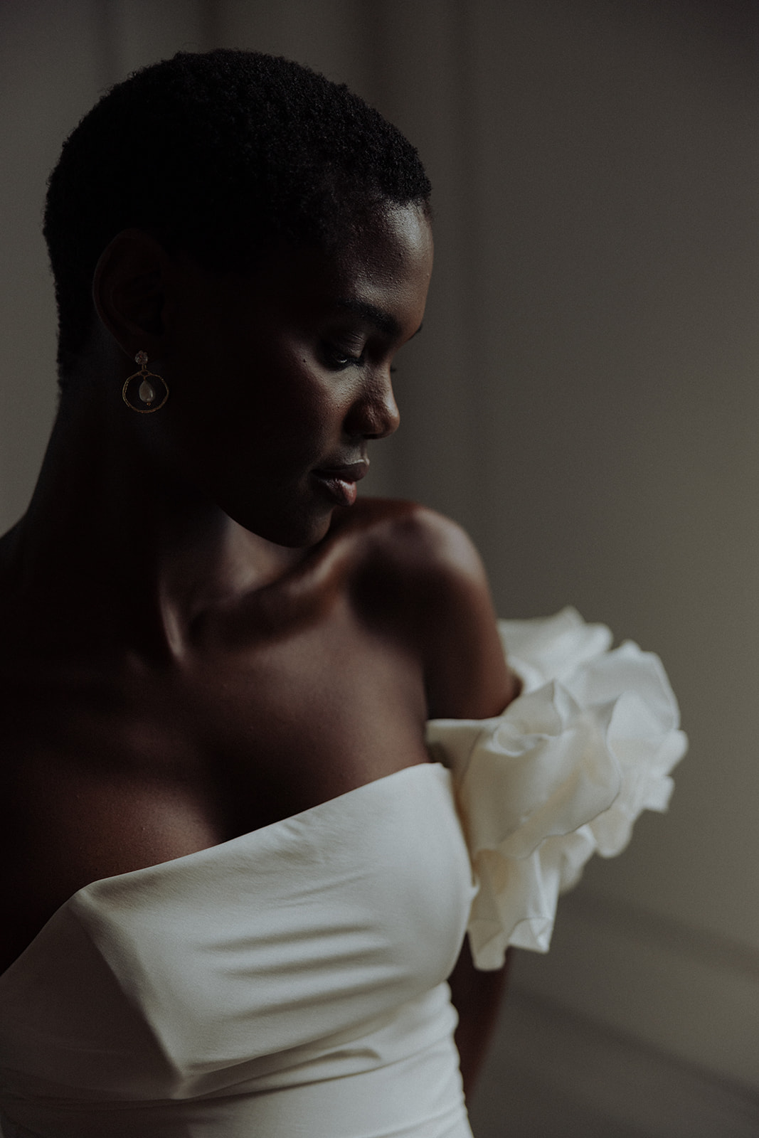 Bride wearing gold statement earrings, side profile in couture gown, editorial wedding portrait.