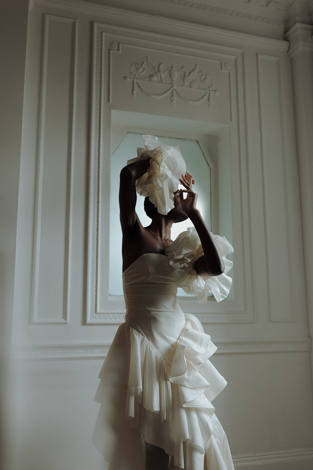 Bride in one-shoulder Darla Haute Couture gown with ruffles, editorial wedding pose by window.