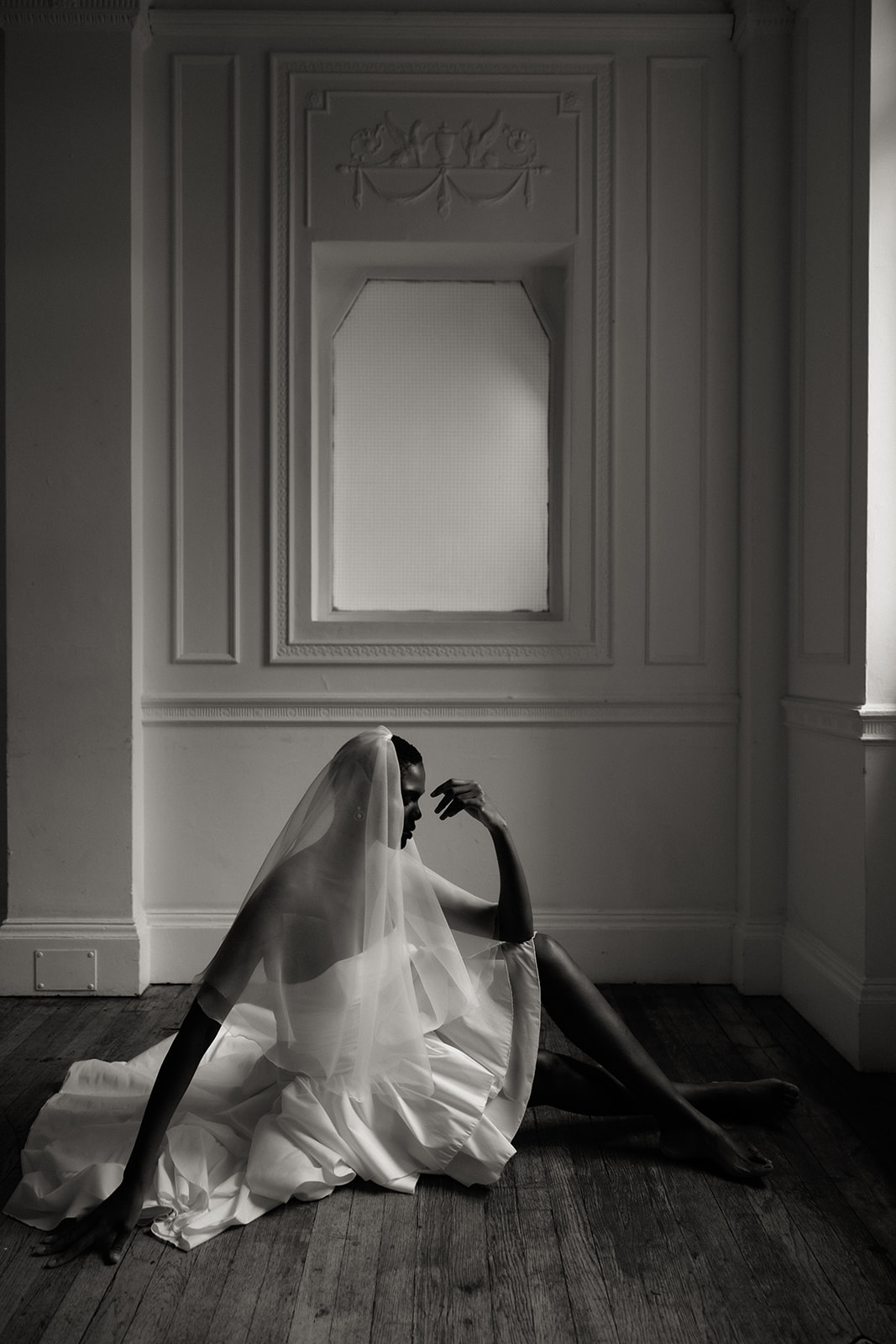 Bride in couture gown with ruffled sleeve seated at window, editorial bridal portrait.