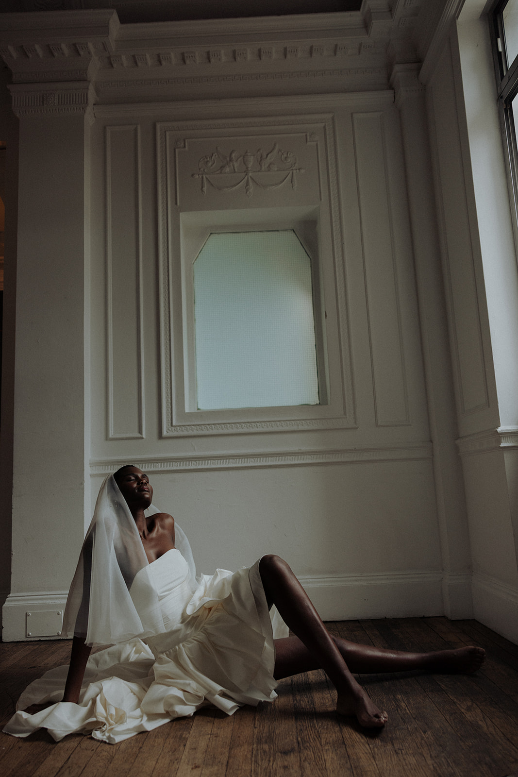 Bride in sculptural Darla Haute Couture gown standing by window, modern editorial photograph.