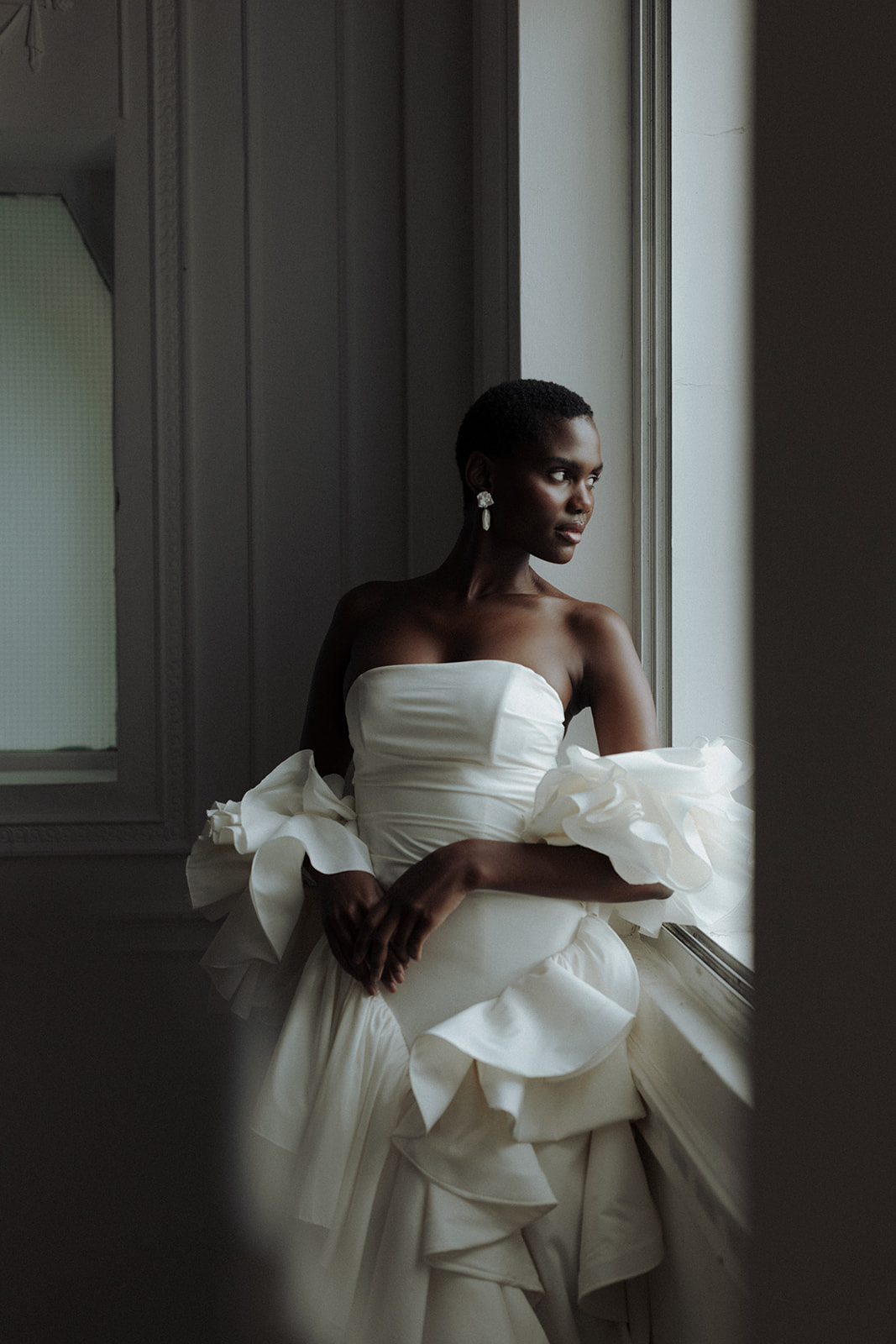 Bride leaning in sculptural couture gown, soft natural light, editorial wedding portrait.