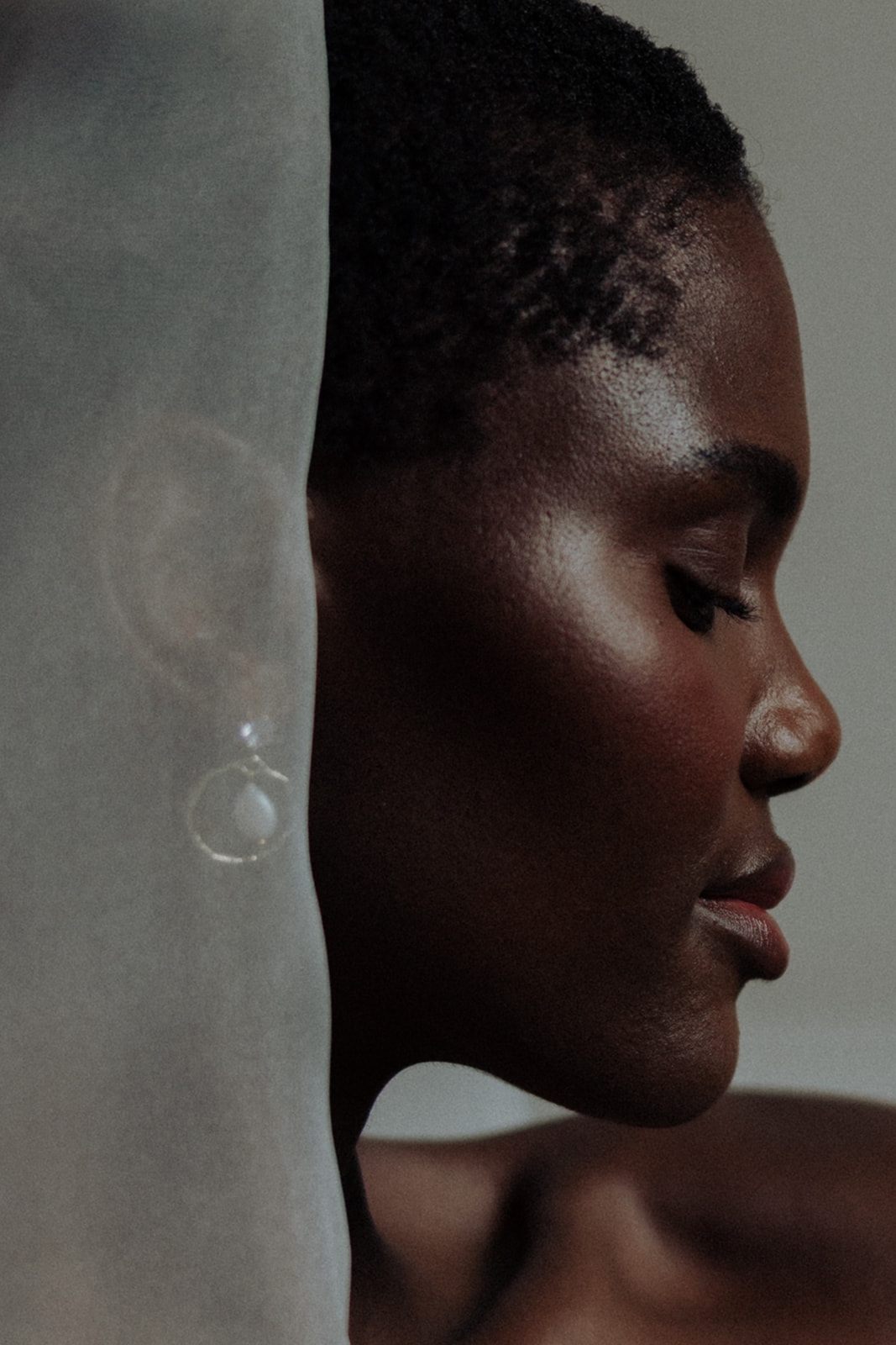 Bride in couture gown wearing luminous earrings, soft profile editorial bridal portrait.