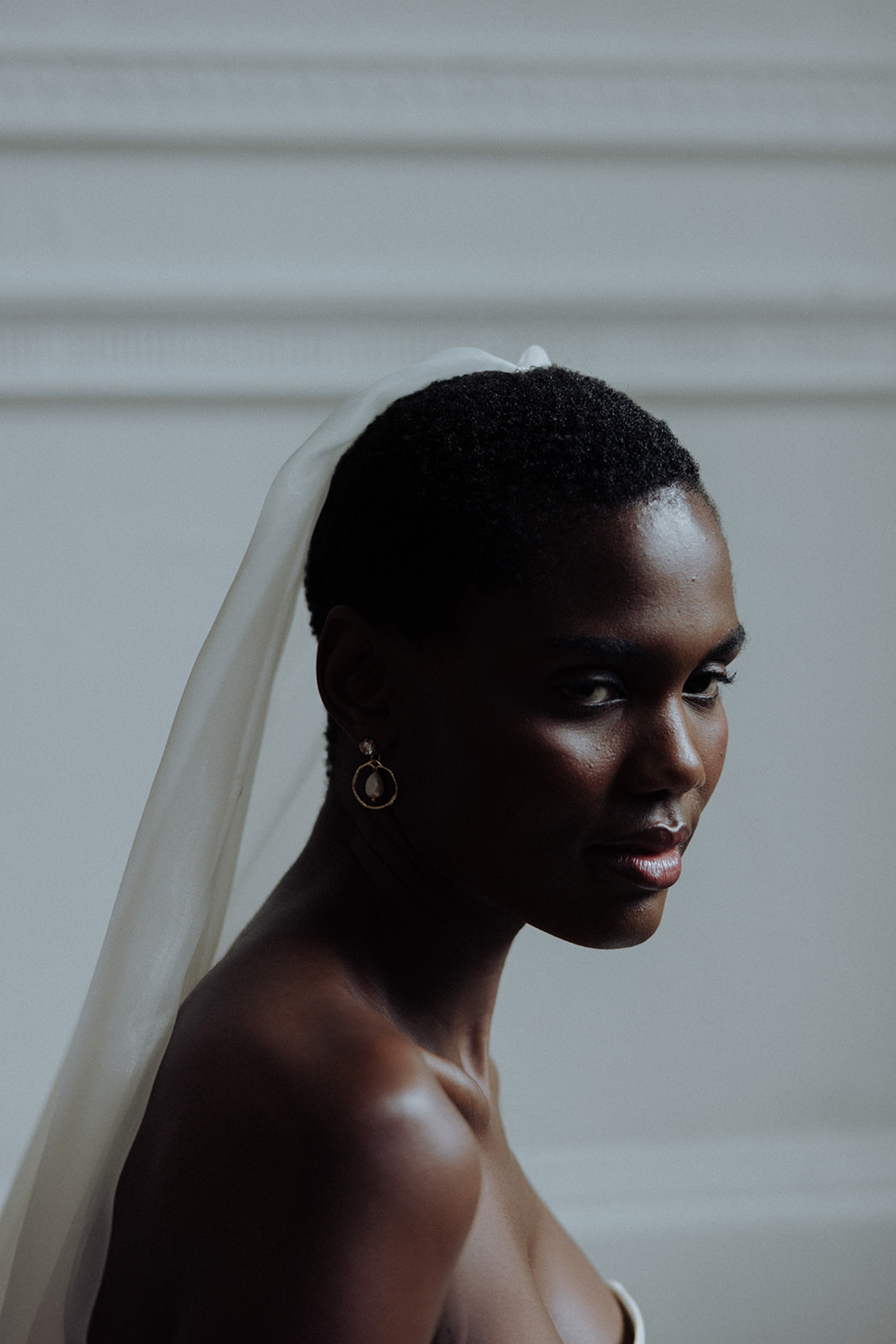 Bride in veil with luminous earrings, soft editorial side portrait.