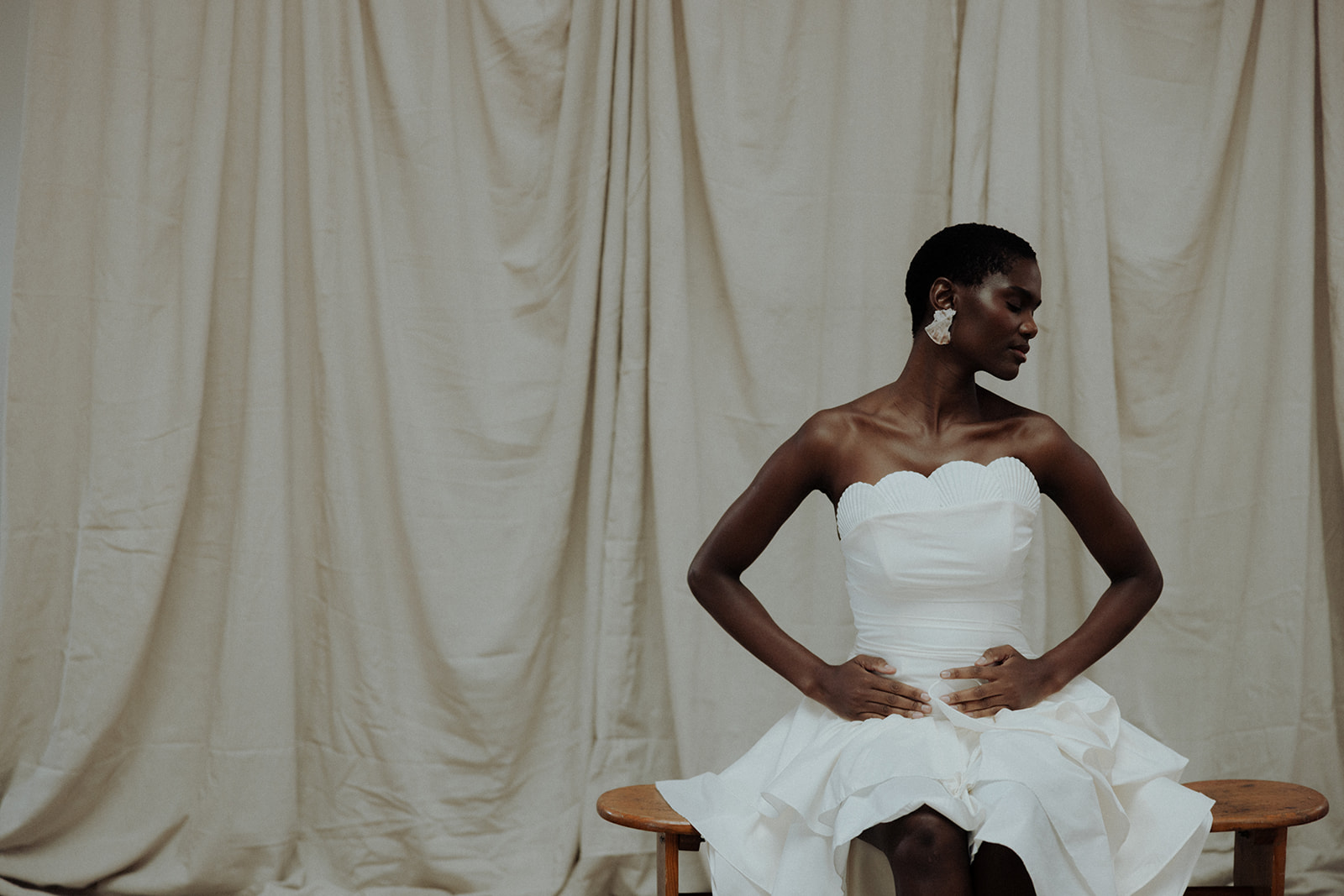 Bride in strapless Darla Haute Couture gown, seated against draped fabric backdrop, editorial bridal portrait.