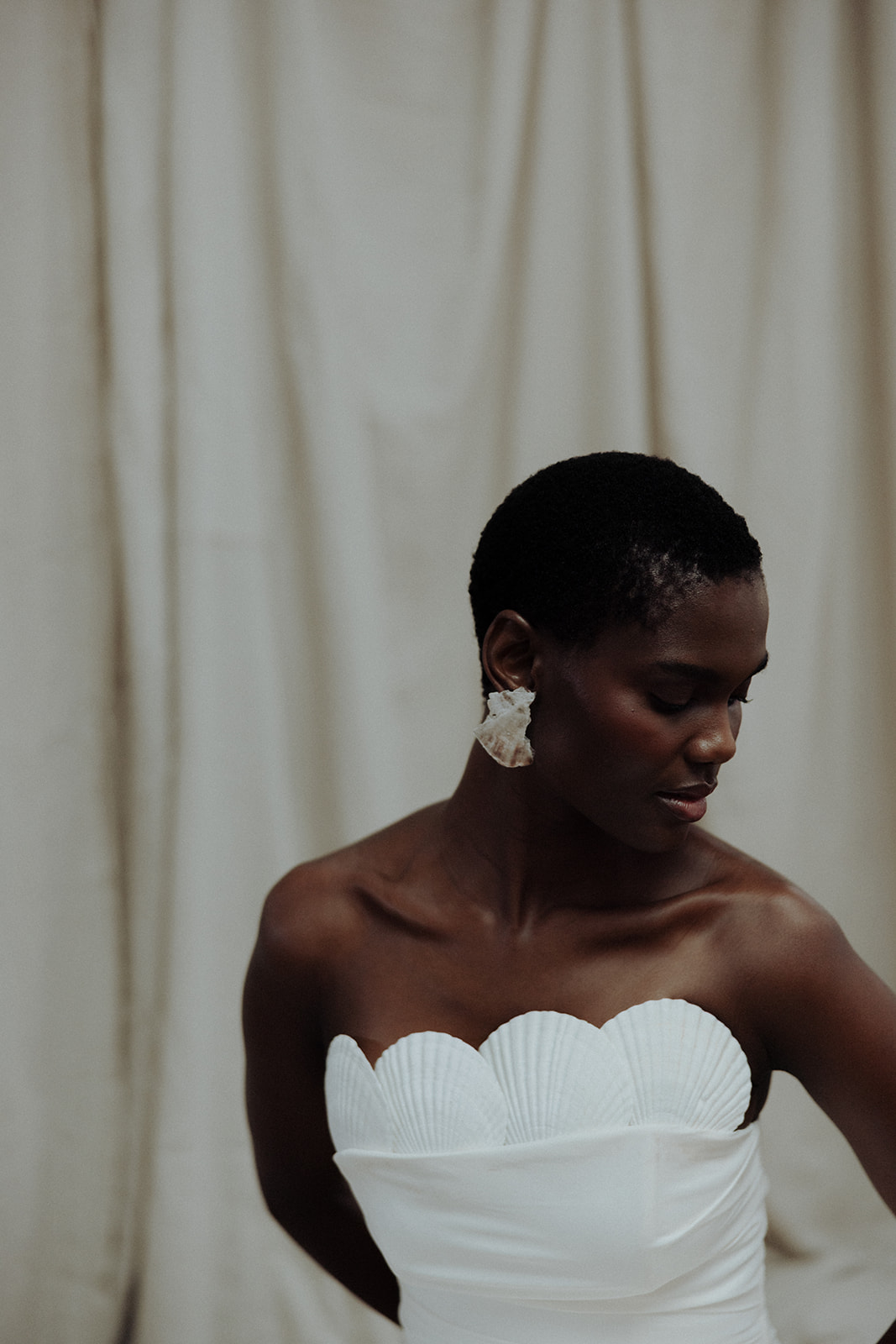 Bride in couture gown wearing oversized floral earrings, editorial bridal close-up.