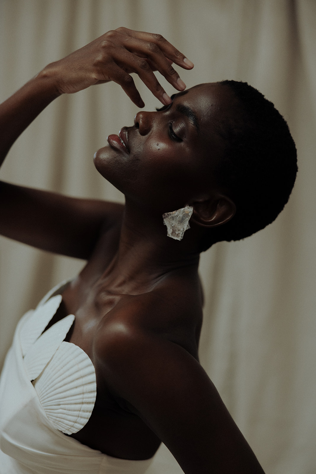 Bride in couture gown wearing floral earrings, head tilted back, editorial bridal portrait.