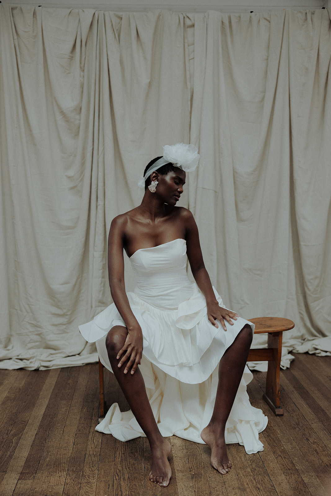 Bride in strapless couture gown with tulle headpiece, seated bridal editorial portrait.