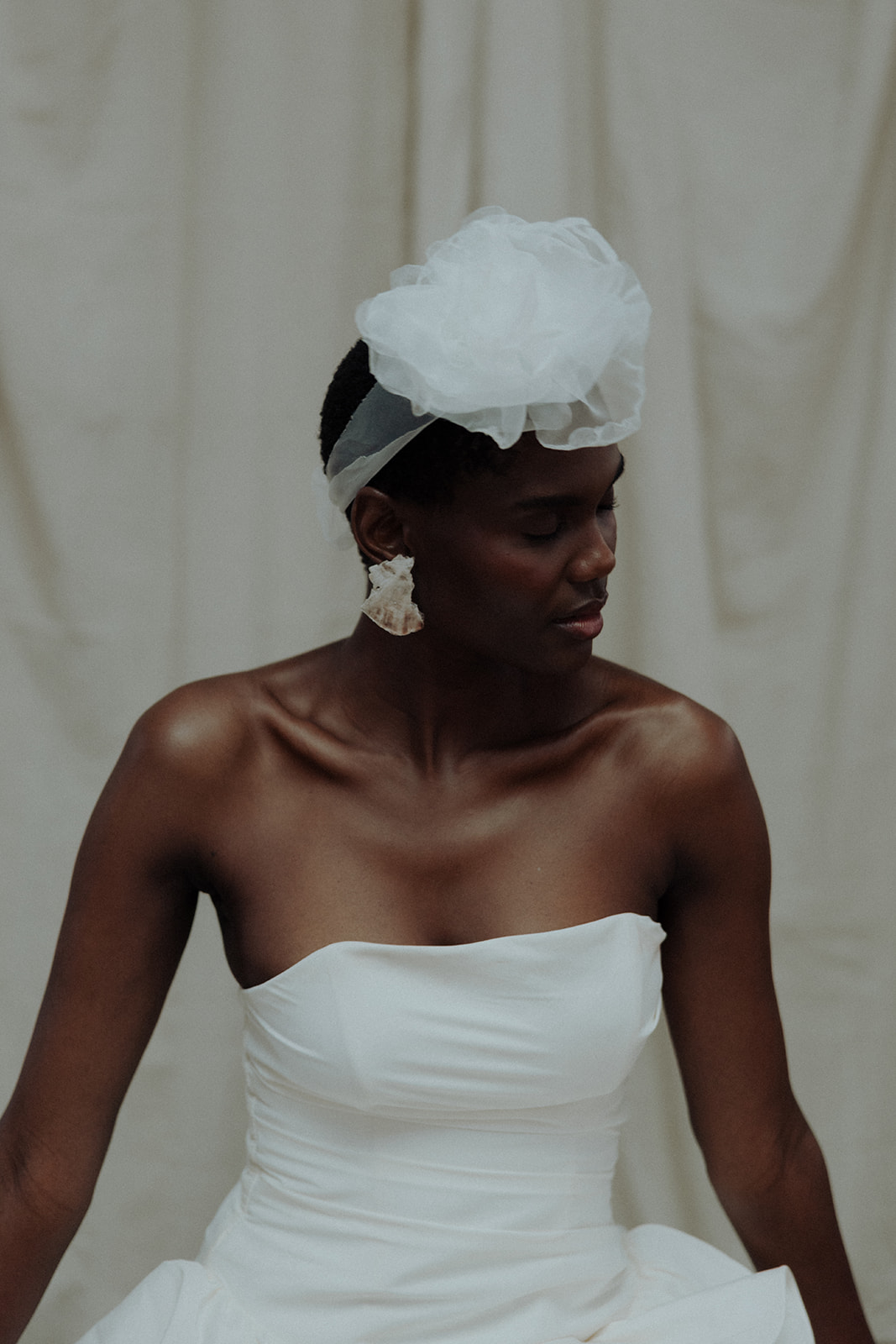 An editorial bridal portrait featuring a strapless couture gown styled with sculptural headpiece and statement earrings.