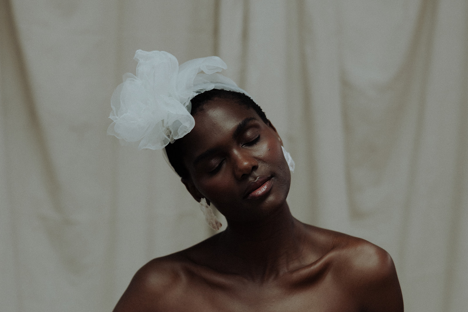 Bride in couture gown and headpiece with draped backdrop, modern editorial bridal portrait.