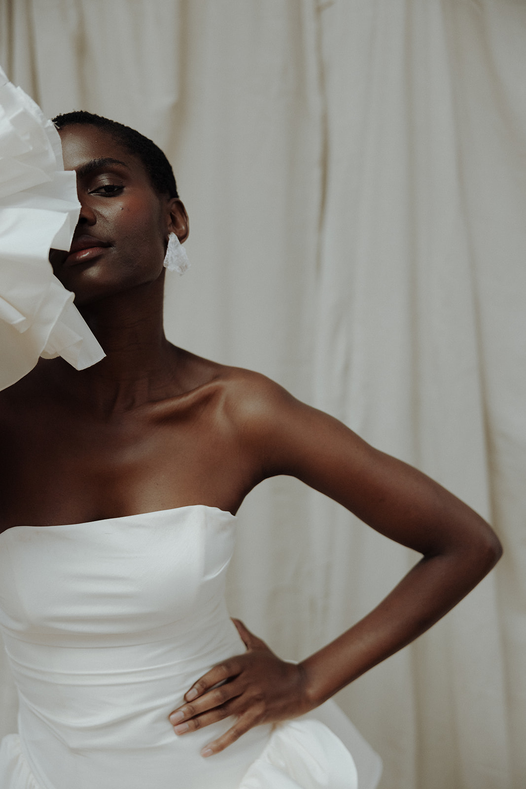 Bride in couture gown with sculptural fabric across face, editorial bridal portrait.