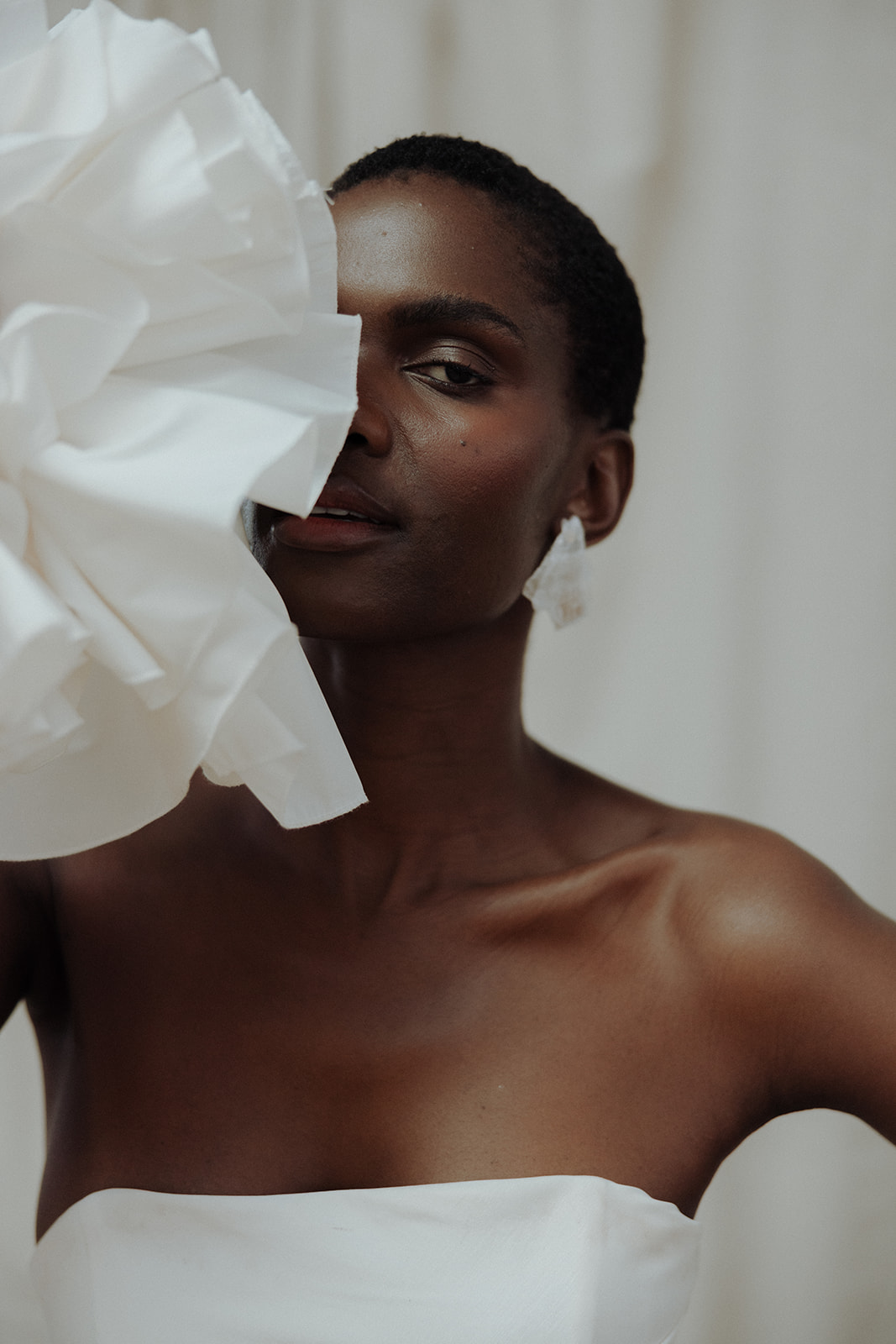 A close-up editorial bridal photograph where ruffled couture fabric frames the bride’s face with cinematic effect.