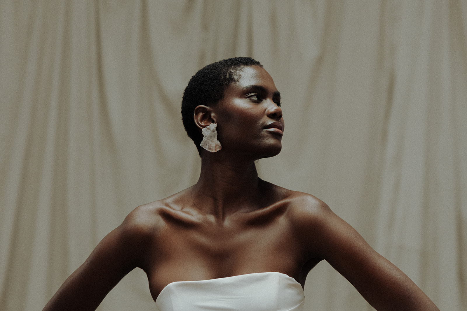 Bride in strapless couture gown, side portrait with curtain backdrop, editorial bridal styling.