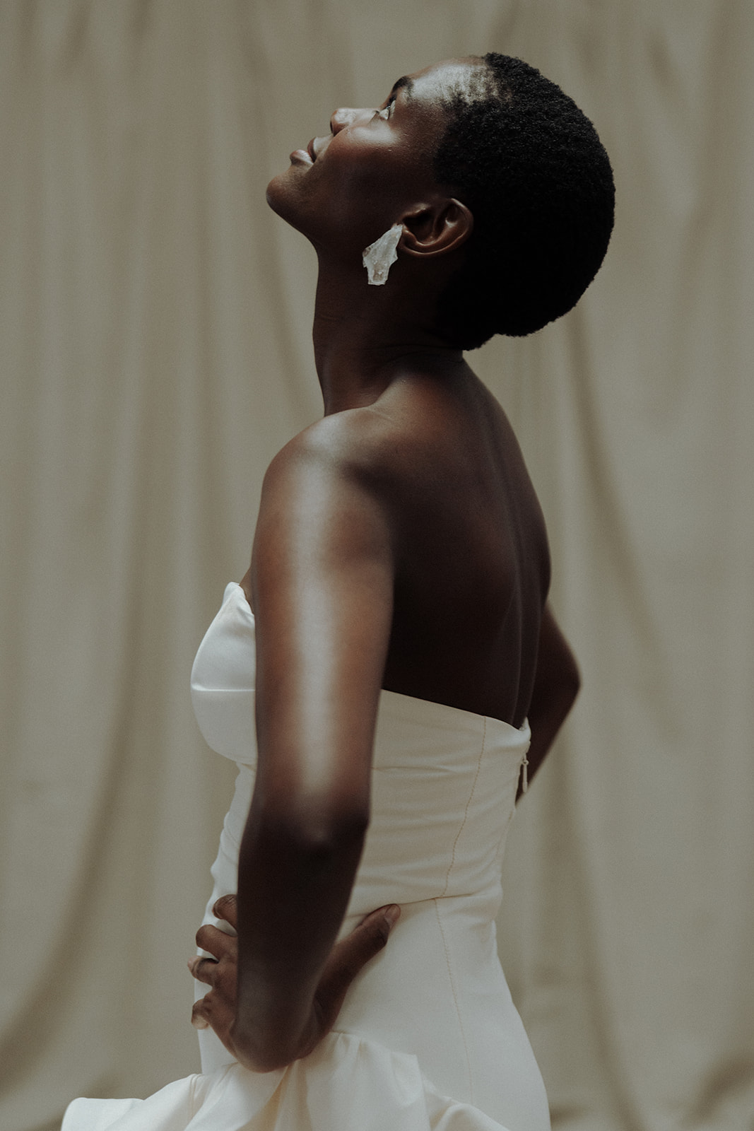 Bride in strapless couture gown, side profile with draped backdrop, editorial bridal portrait.