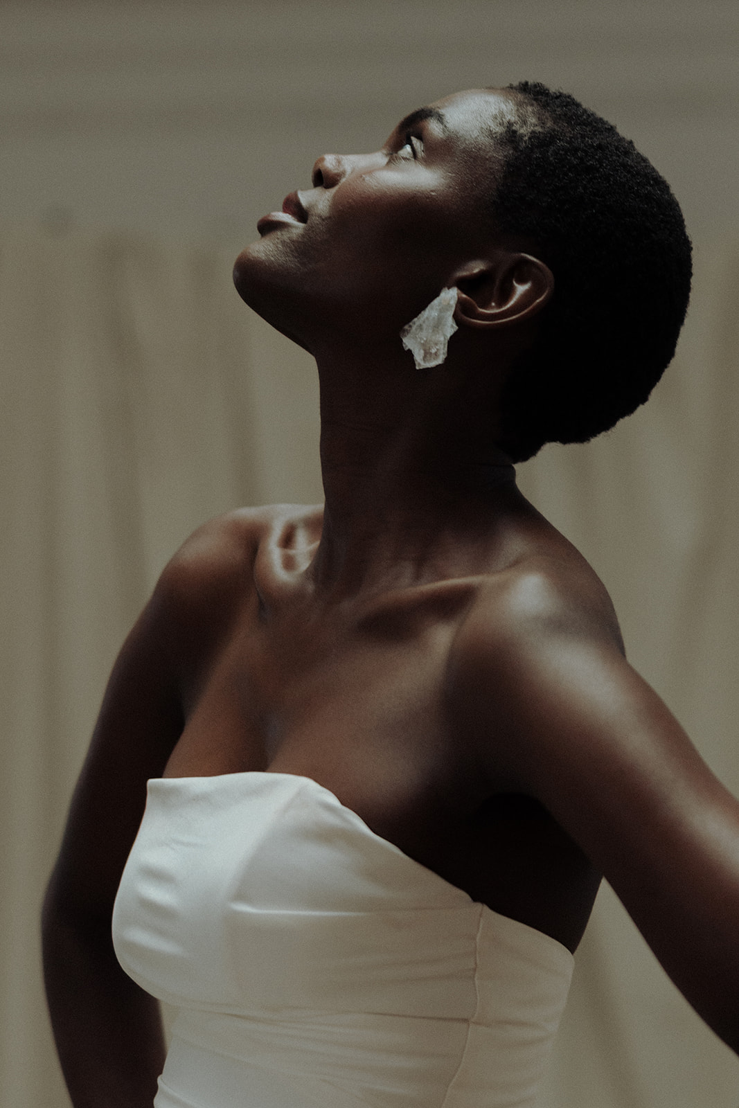 Bride in strapless couture gown wearing statement earrings, close-up editorial portrait.