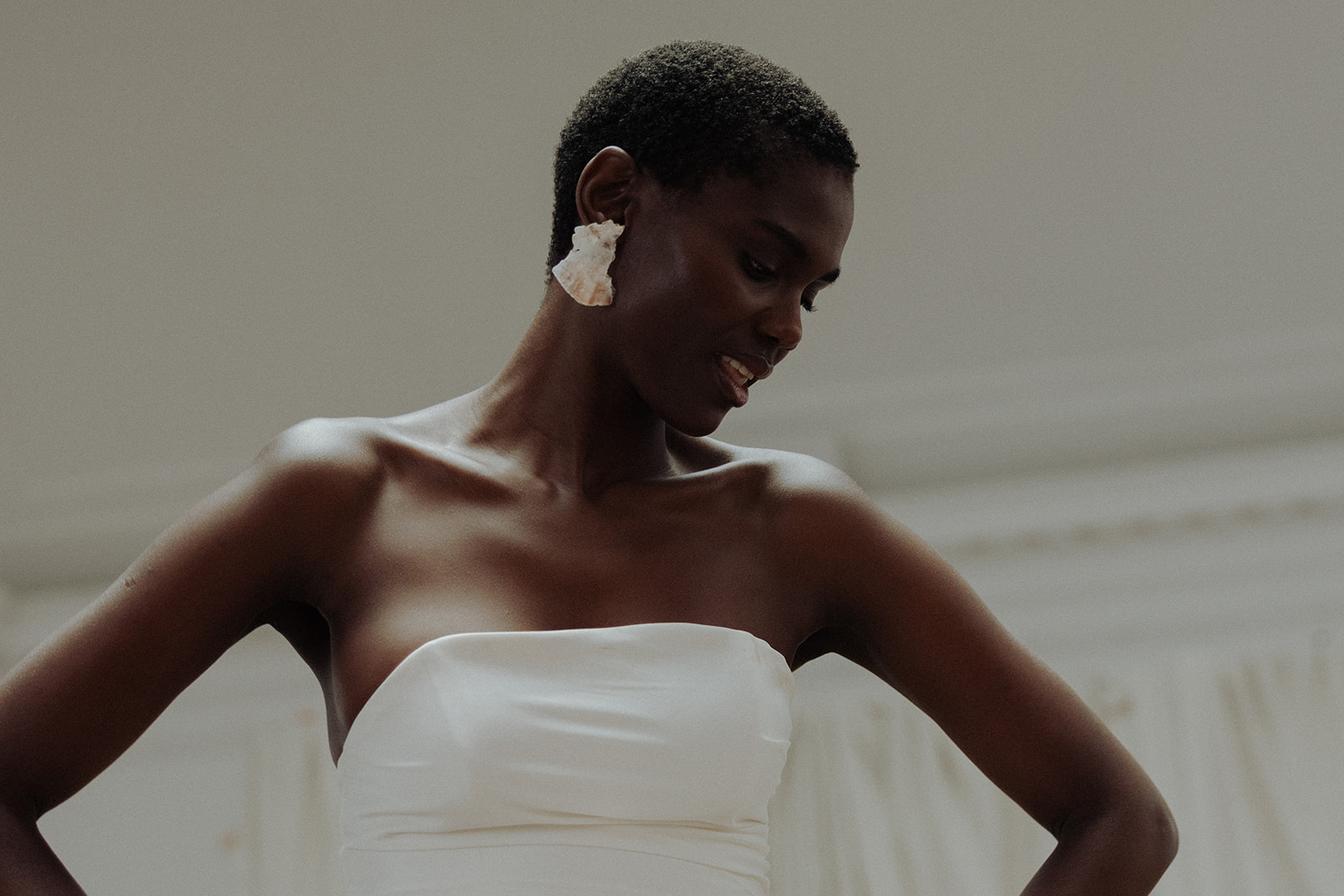 Bride in strapless couture gown wearing floral earrings, looking down, editorial portrait.