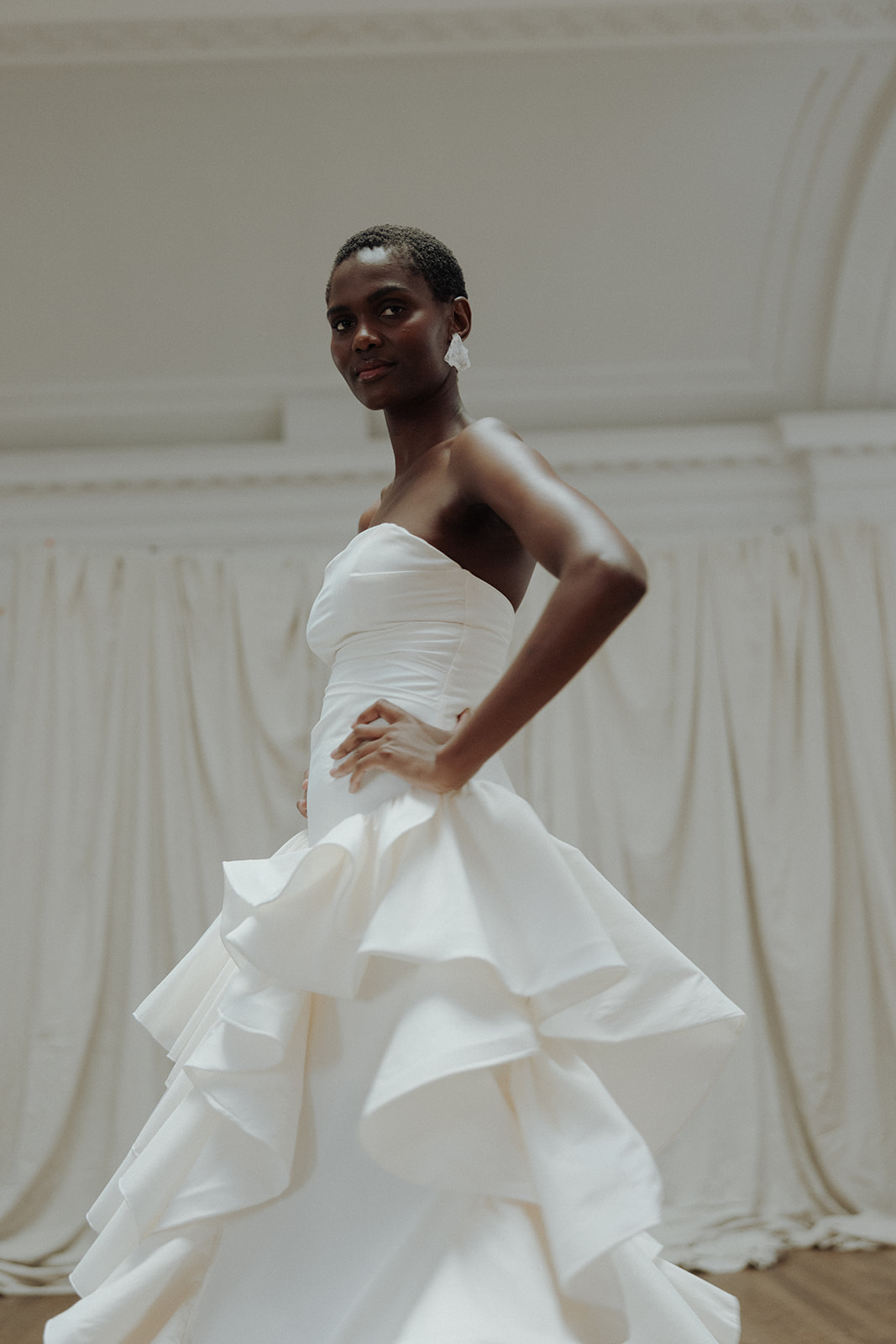 Bride in strapless couture gown with ruffled hem, standing with hands on hips, editorial bridal portrait.