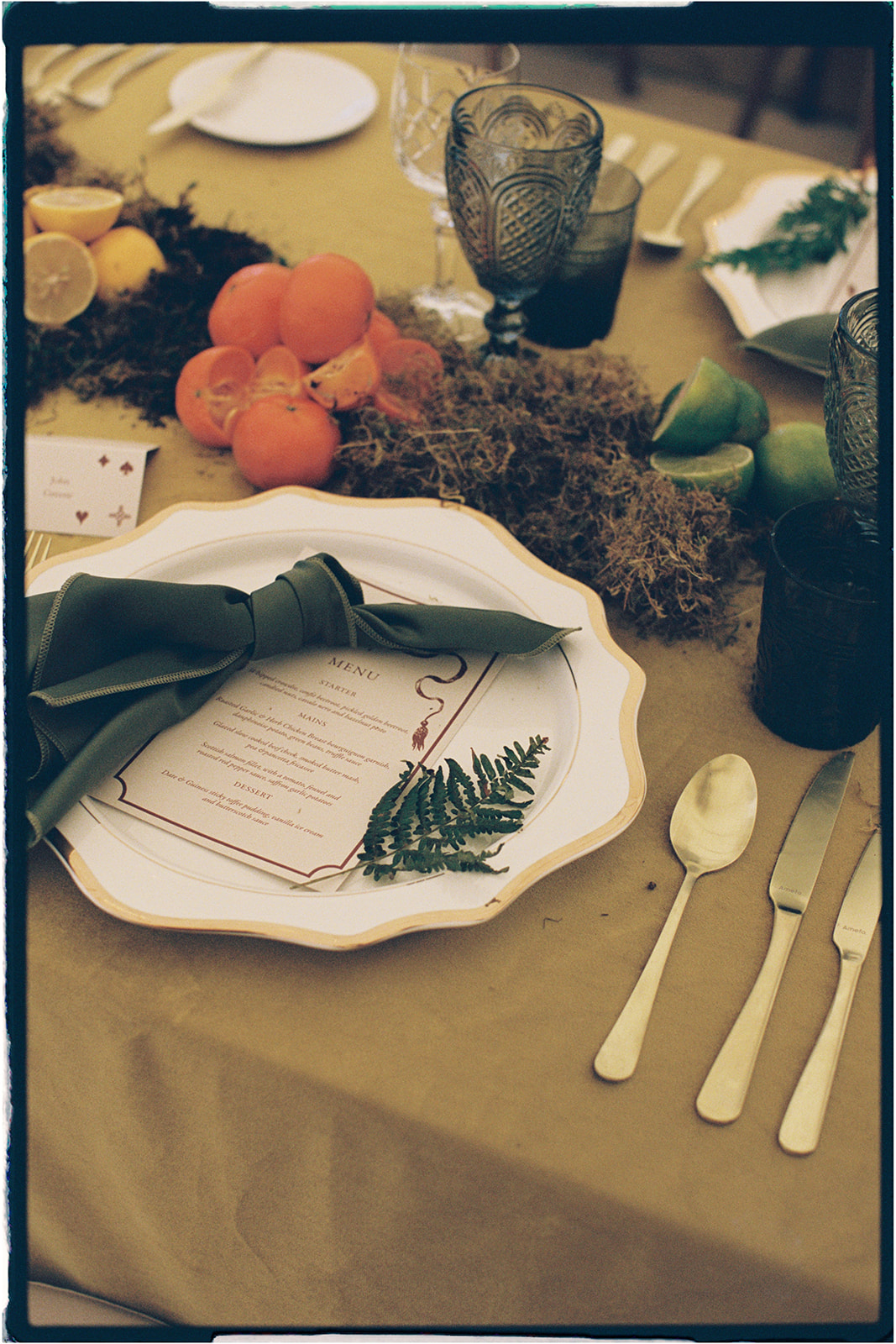 Elegant wedding table setting with moss, fern sprig, and handwritten menu styled by Tupelo Tree at Winton Castle.