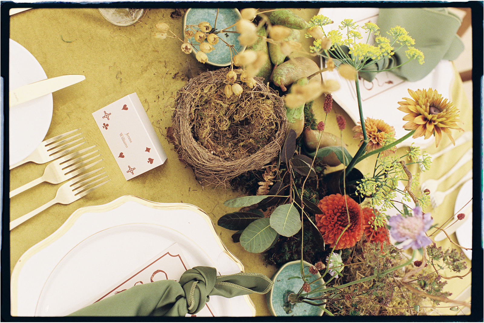 Artistic tablescape detail featuring a small bird’s nest and soft seasonal flowers, photographed on 35mm film.